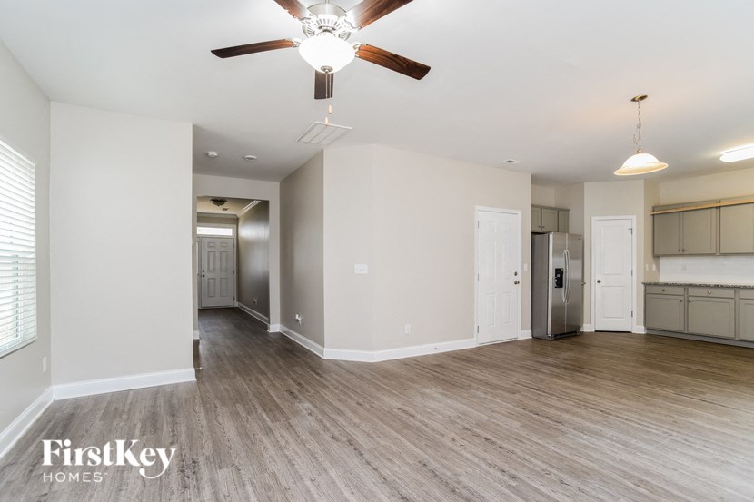 A spacious room with a ceiling fan and light fixture, and a kitchen area with a refrigerator and cabinets.