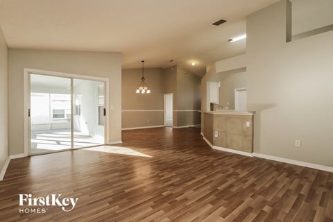 an empty living room with wood flooring and a door to the kitchen