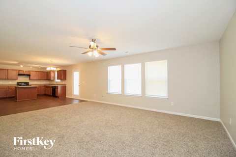 an empty living room with a ceiling fan and a kitchen
