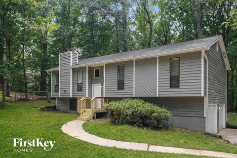 A house with a grey siding and a white door is surrounded by greenery.