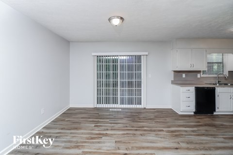 A spacious room with a window, wooden floor, and a kitchenette.