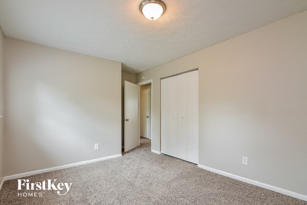 a bedroom with white walls and carpet and a door to a closet