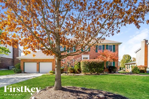 A tree with orange leaves stands in front of a house with a sign that says "FirstKey Homes.".