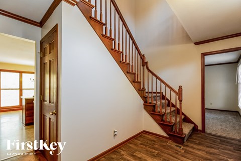 A staircase with a wooden handrail and steps leading up to a landing with a white wall and a doorway.