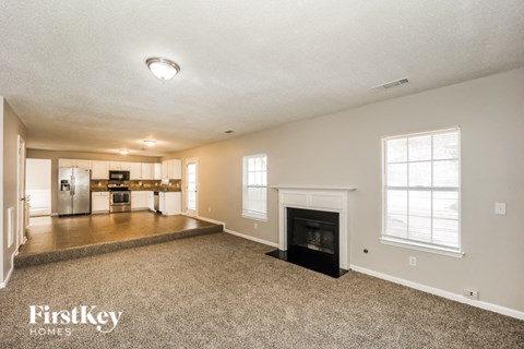 A spacious living room with a fireplace and a kitchen in the background.