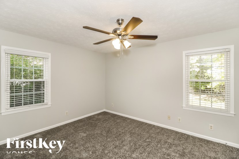 A room with a ceiling fan and two windows.