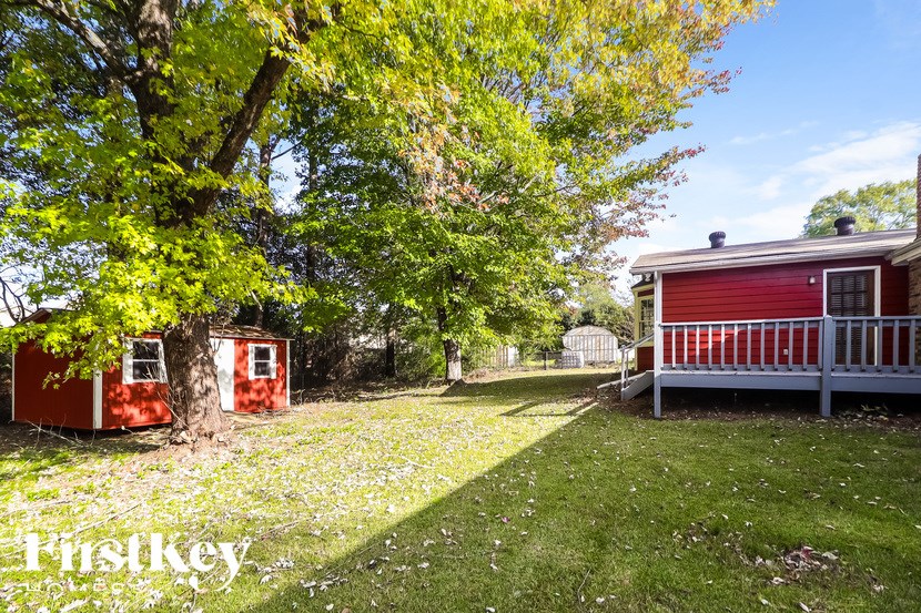 A red shed sits in a grassy field next to a tree.