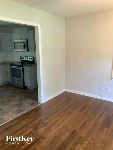 A kitchen with a microwave, oven, and stove top is visible through a doorway into a living room.
