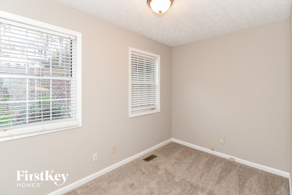 A room with a carpeted floor, a window with blinds, and a light fixture on the ceiling.
