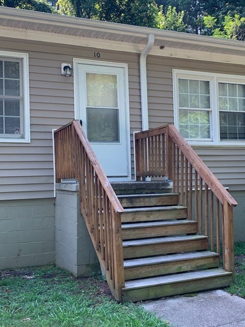 A house with a grey siding and a white door has a wooden staircase leading to the front door.