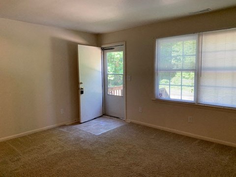 A room with a carpeted floor, a door, and a window with blinds.