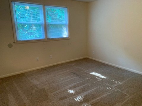 A room with a carpeted floor and a window with blinds.