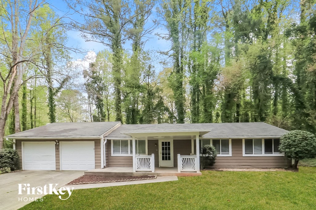 A house with a porch and a garage is surrounded by trees.
