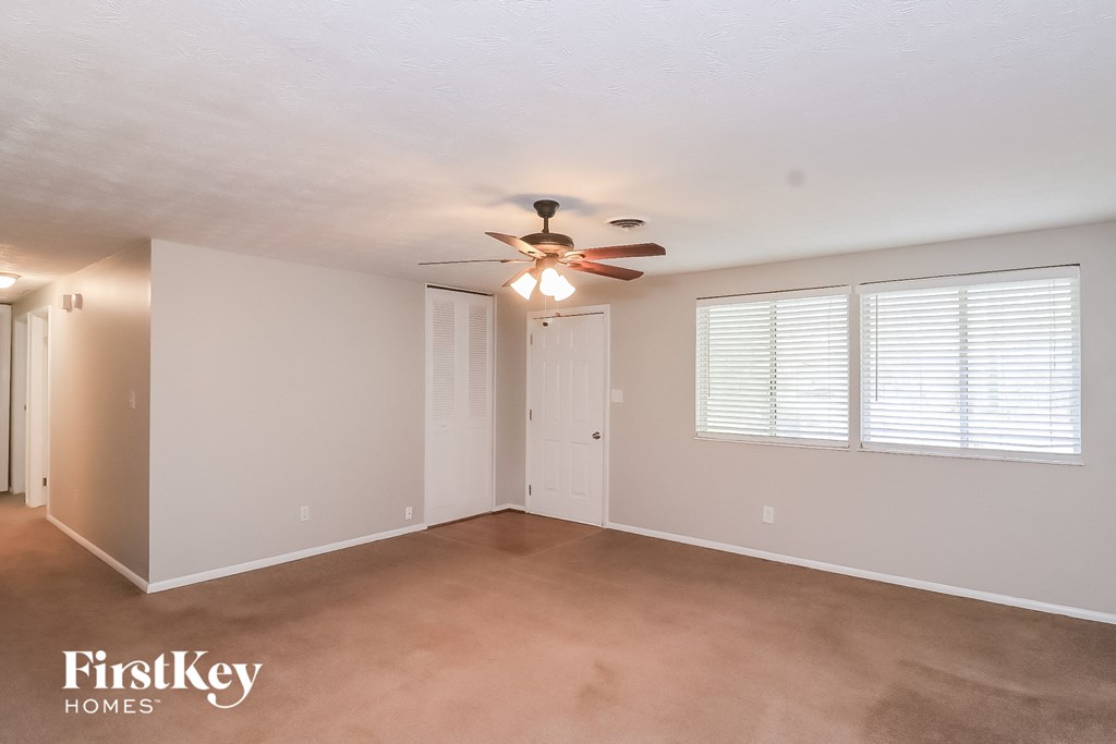 A spacious room with a ceiling fan and two windows with blinds.