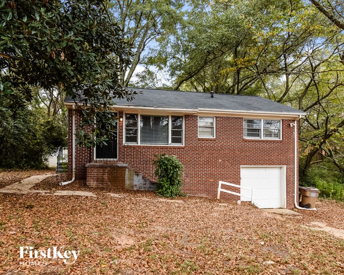 A brick house with a white garage door is surrounded by trees.