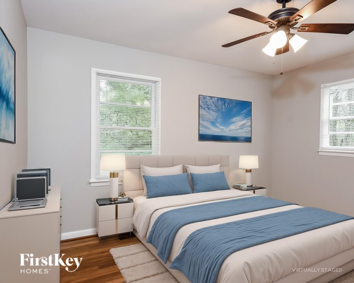 A bedroom with a bed, two lamps, a ceiling fan, and a painting on the wall.