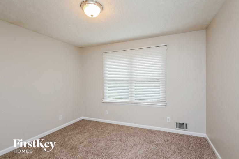 the spacious bedroom has carpeted floors and a large window