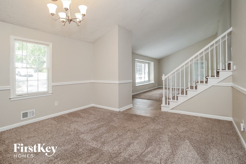 a carpeted living room with a staircase and a window