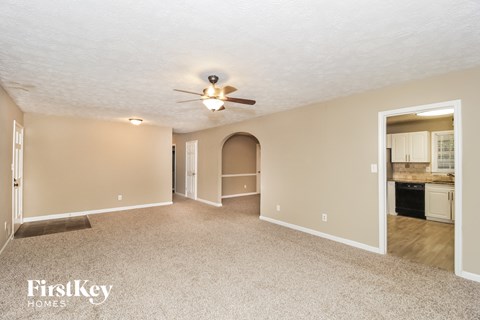 an empty living room with a ceiling fan and a kitchen