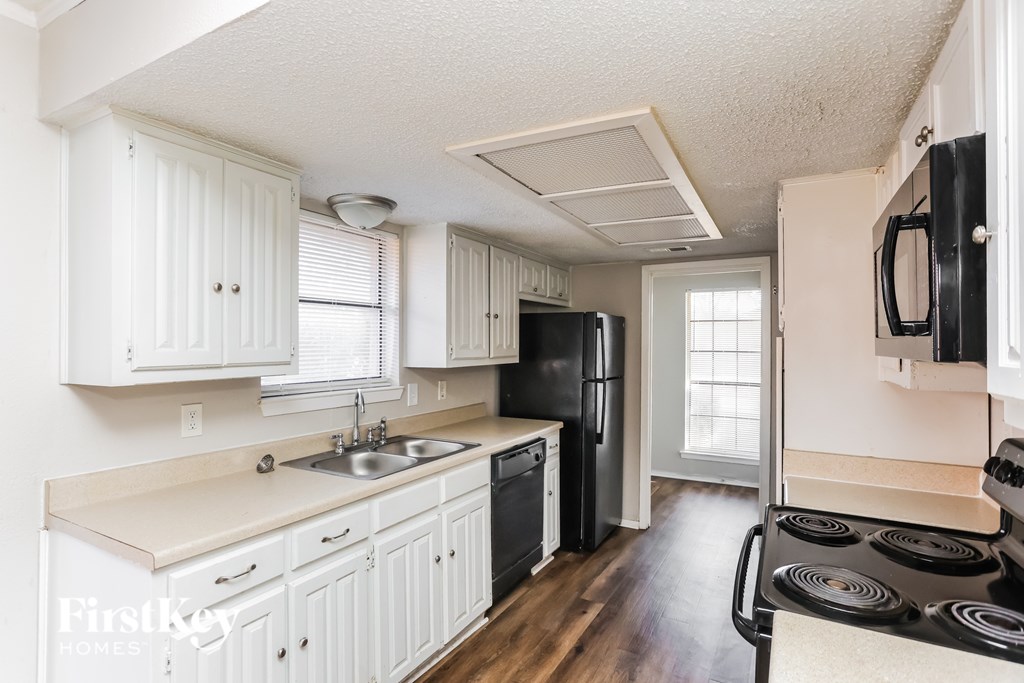 A kitchen with white cabinets and a black refrigerator.