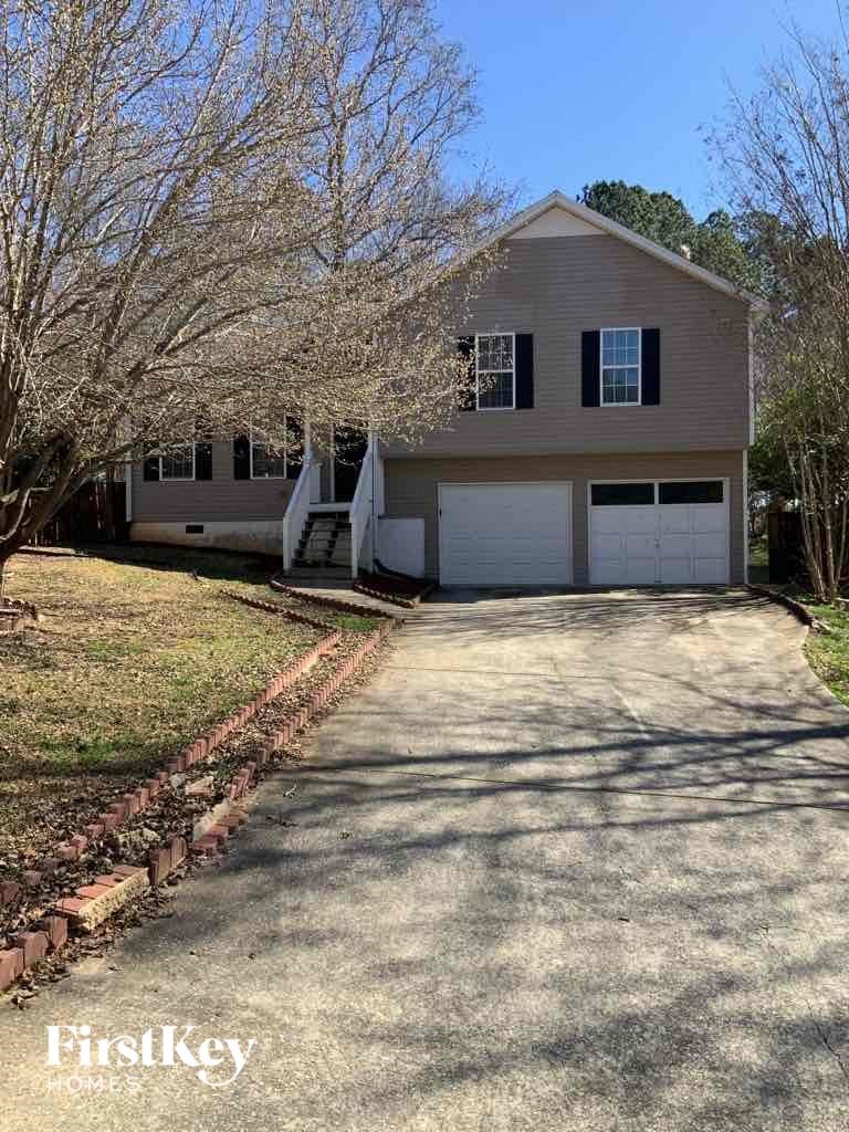 A two-story house with a garage is surrounded by trees and has a driveway leading to the front door.