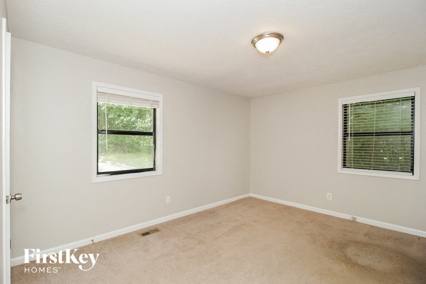 an empty bedroom with two windows and a carpeted floor