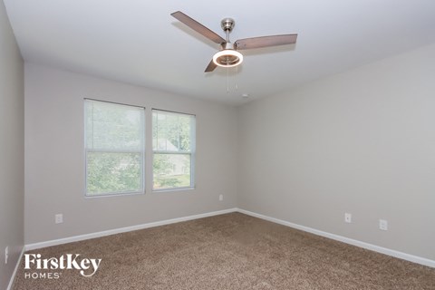 an empty room with a ceiling fan and two windows