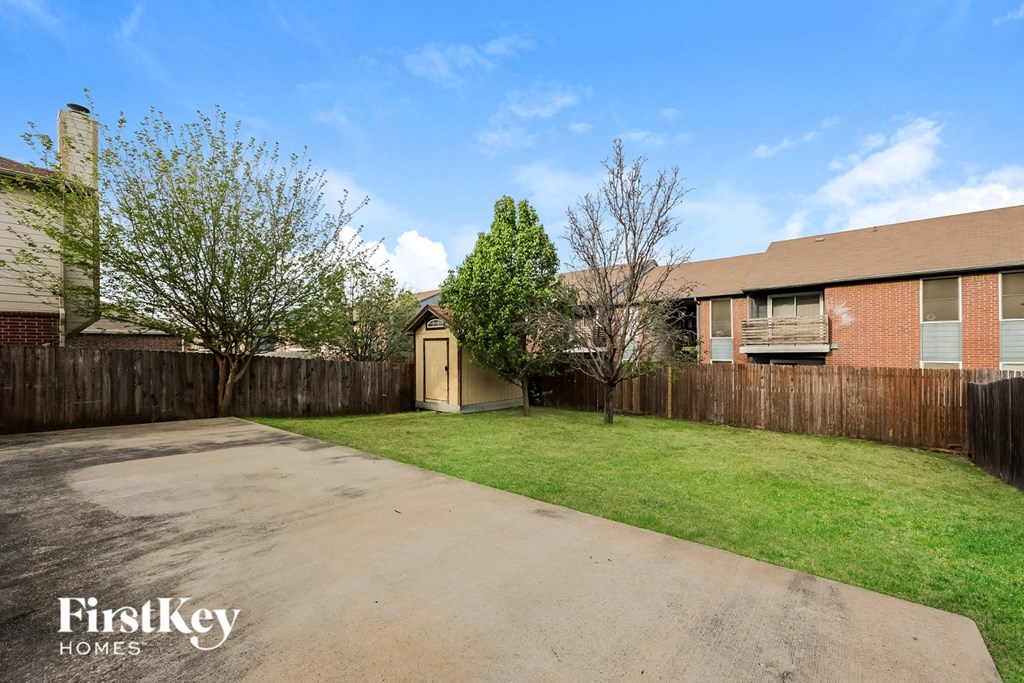 A backyard with a driveway, a tree, and a fence.