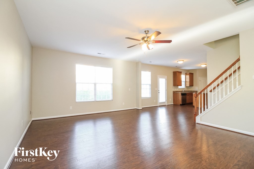 A spacious room with a wooden floor and a staircase on the right side.