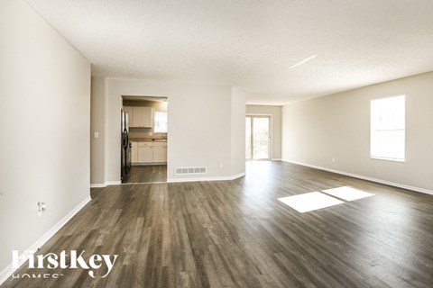A spacious room with wooden floors and white walls, with a view of a kitchen in the distance.