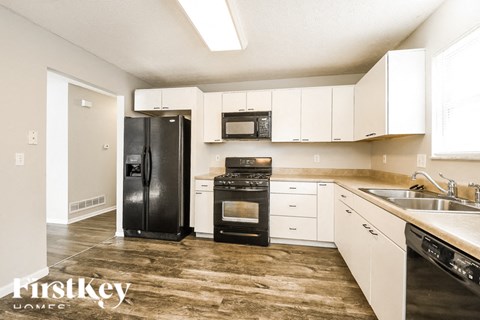 A kitchen with a black refrigerator, black oven, and white cabinets.