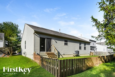 A house with a grey siding and a black door is surrounded by a wooden fence.