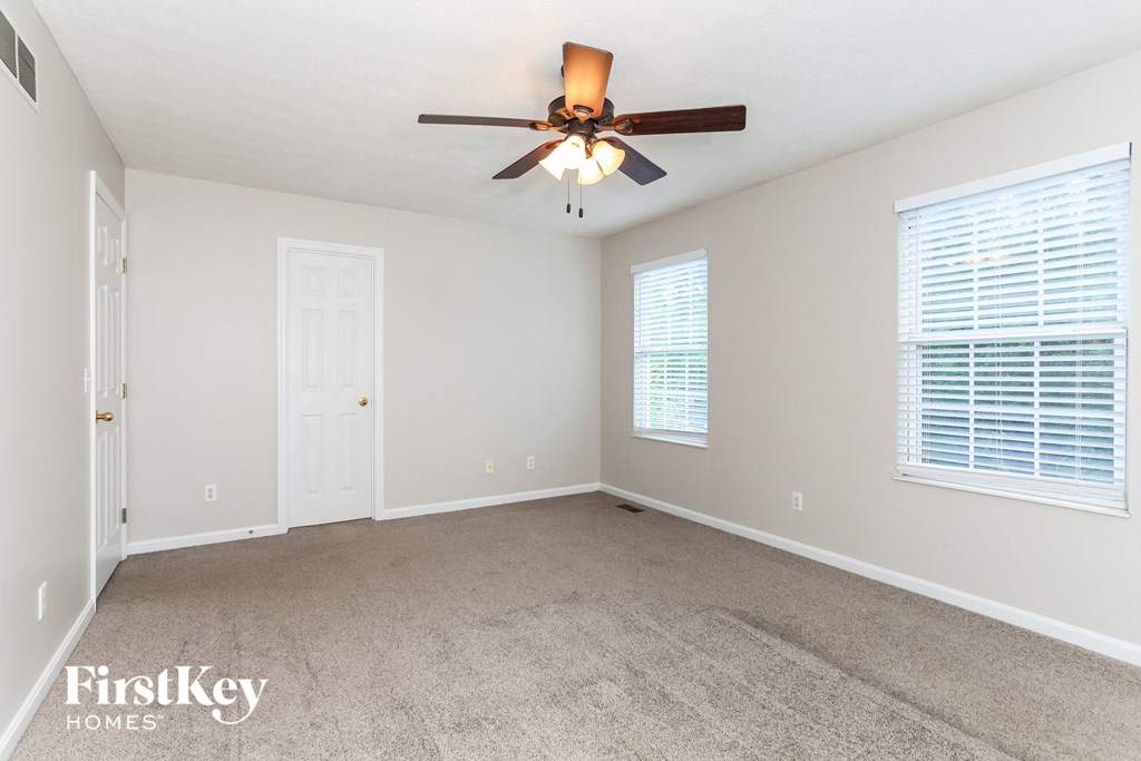 A spacious room with a ceiling fan and two windows.