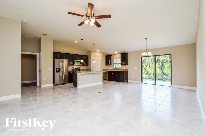 A spacious, empty room with a ceiling fan and a kitchen area in the background.