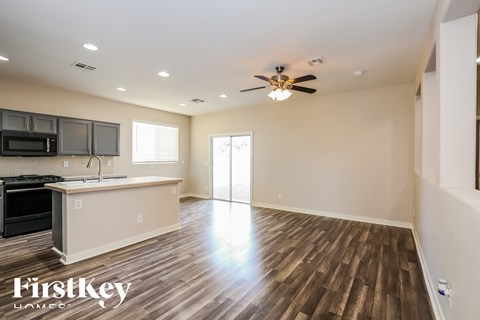 A spacious kitchen and living room with wood flooring and a ceiling fan.