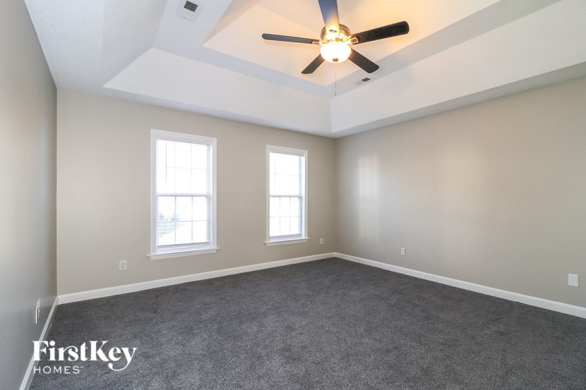 A spacious room with a ceiling fan and two windows.