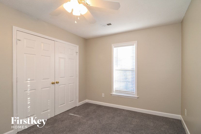 A bedroom with a white door, a window with blinds, and a ceiling fan.