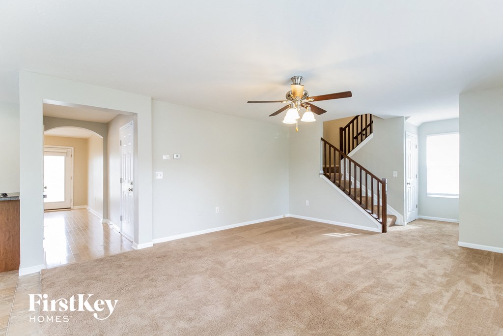 A spacious living room with a staircase and a ceiling fan.