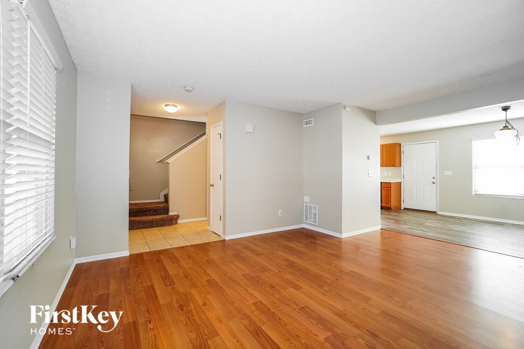 A room with wooden floors and white walls, with a staircase leading to another room.