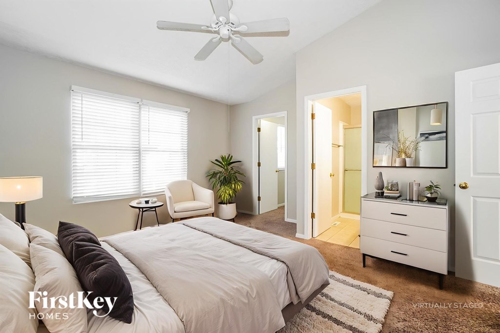 A bedroom with a bed, a chair, a side table, a dresser, and a mirror.