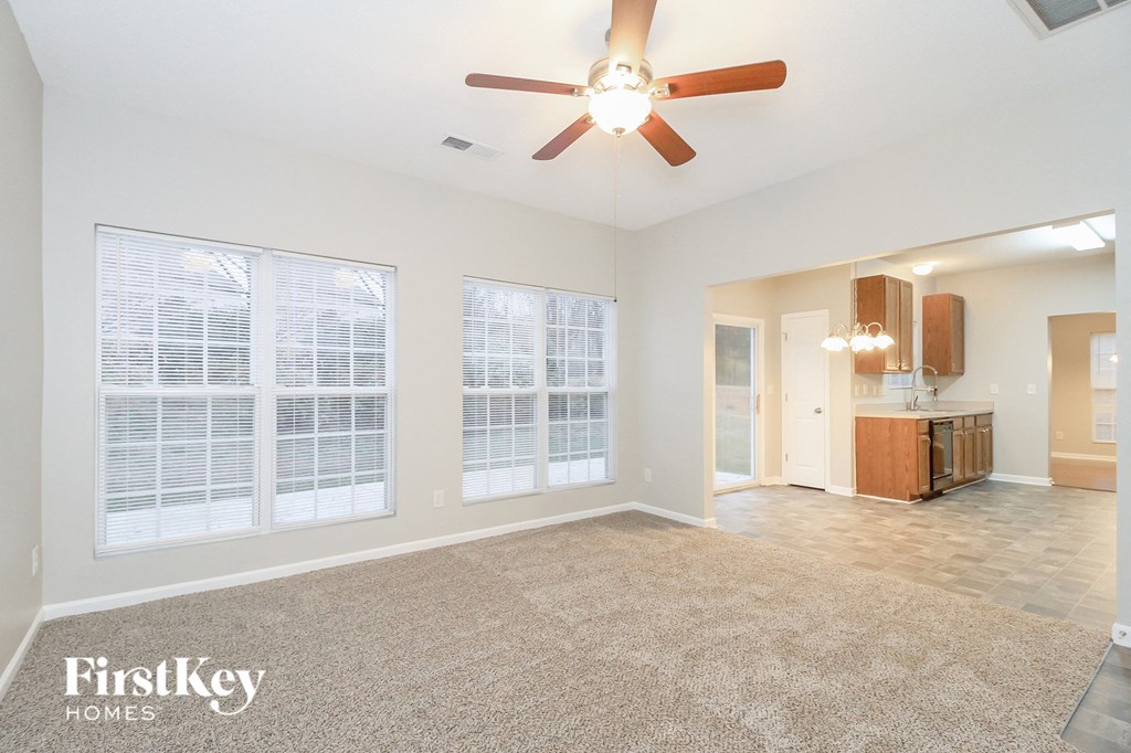 an empty living room with a ceiling fan and a kitchen