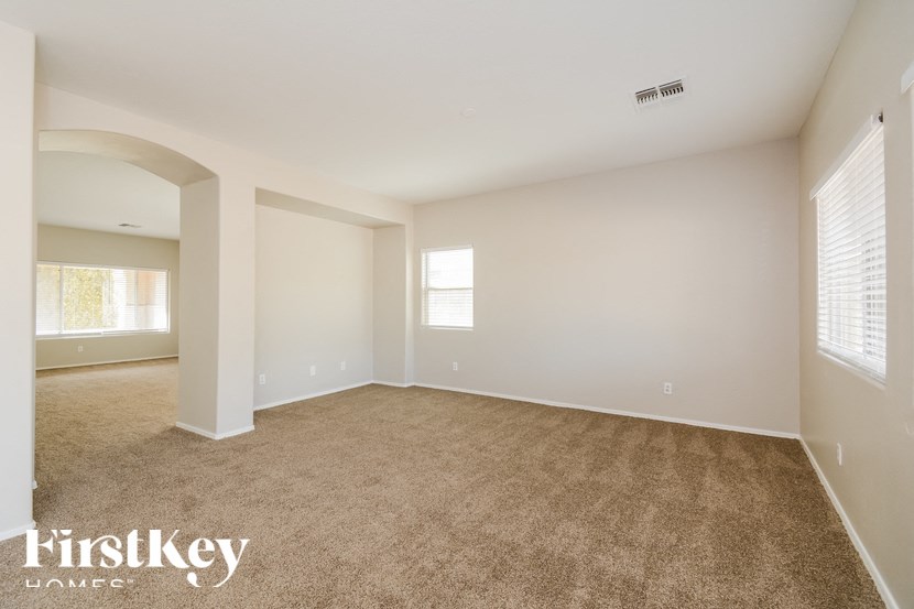 A spacious room with beige carpeting and white walls, with a window on the right side.