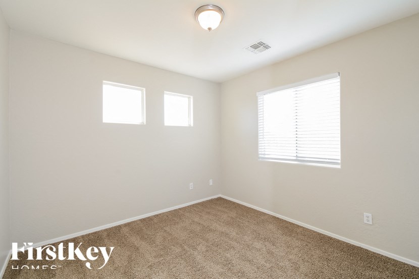 A room with a carpet floor, two windows, and a ceiling light.