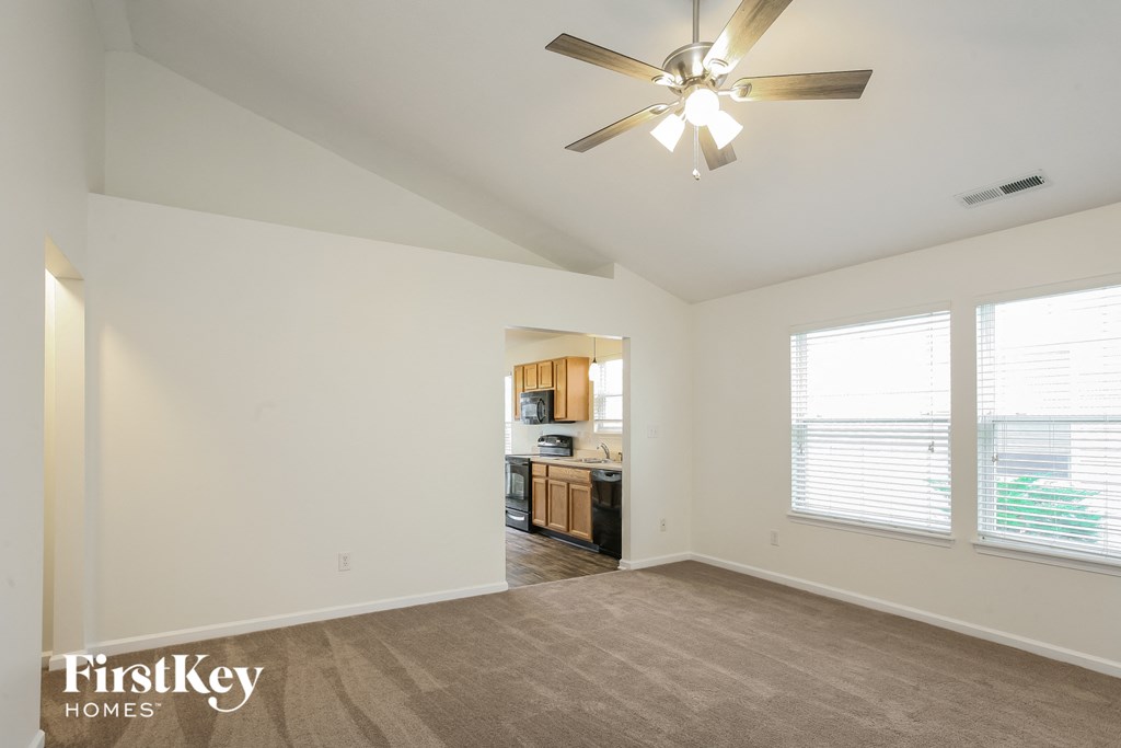an empty living room with a ceiling fan and a kitchen