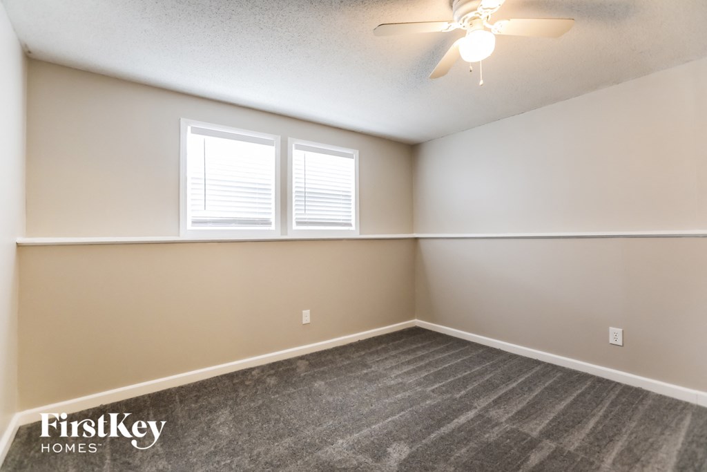 the living room of an empty house with a ceiling fan and two windows