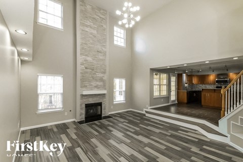A spacious living room with a stone fireplace and a staircase leading to the upper floor.