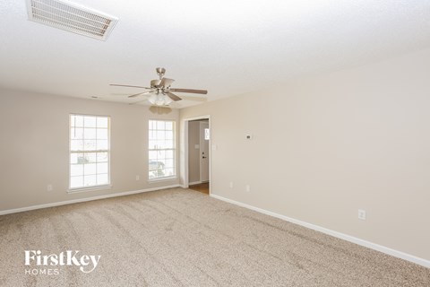 A spacious room with a carpeted floor, a ceiling fan, and a door leading to another room.
