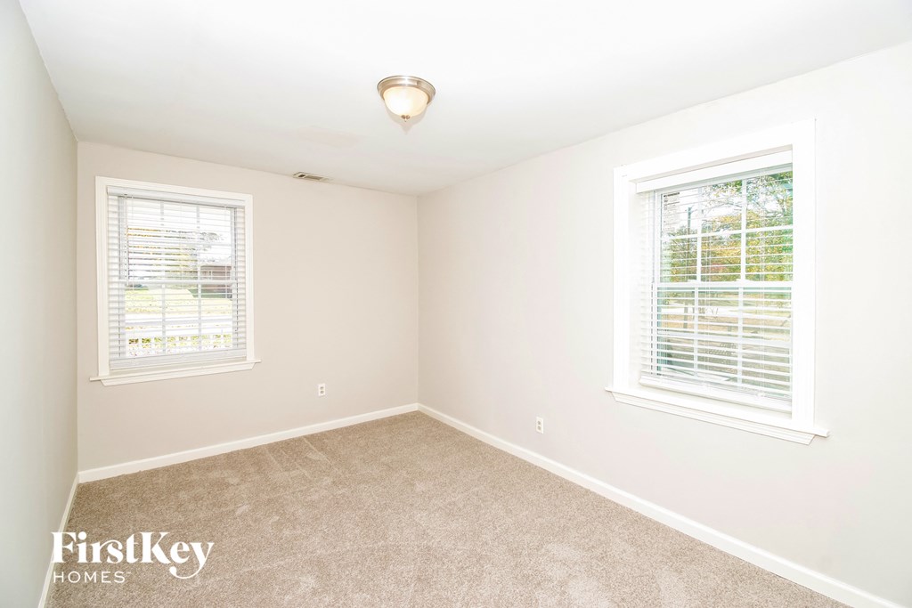 a bedroom with two windows and beige carpet and white walls
