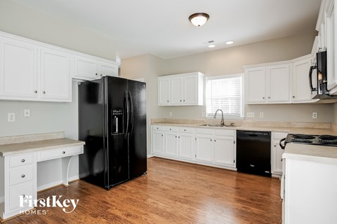 A black refrigerator in a kitchen with white cabinets.