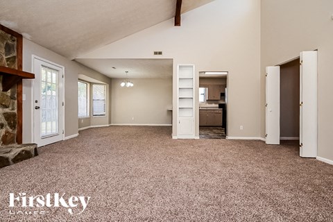 A spacious room with a carpeted floor and a stone fireplace on the left side.